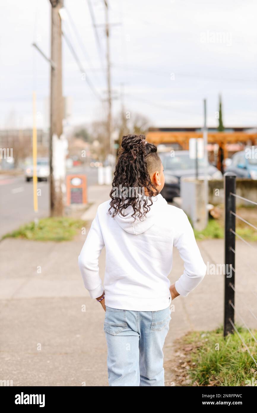 Young kid with long curly hair walking down city sidewalk Stock Photo