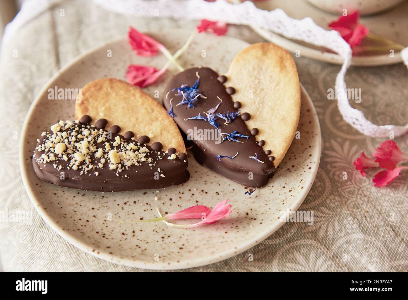 Vegan heart shaped cookies among flowers. Romantic holiday food background. Stock Photo