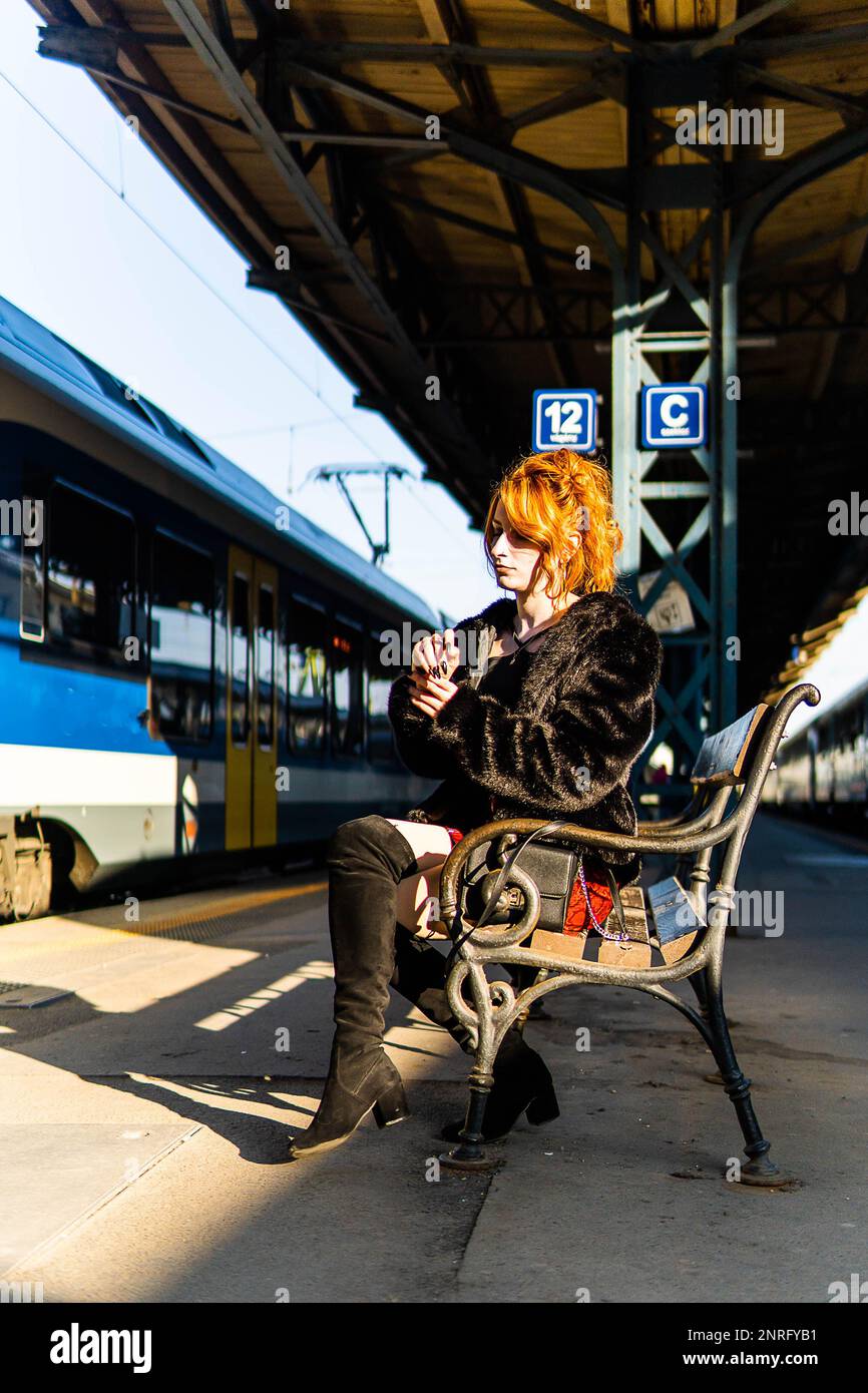 red-haired woman in train station waiting in a bench Stock Photo