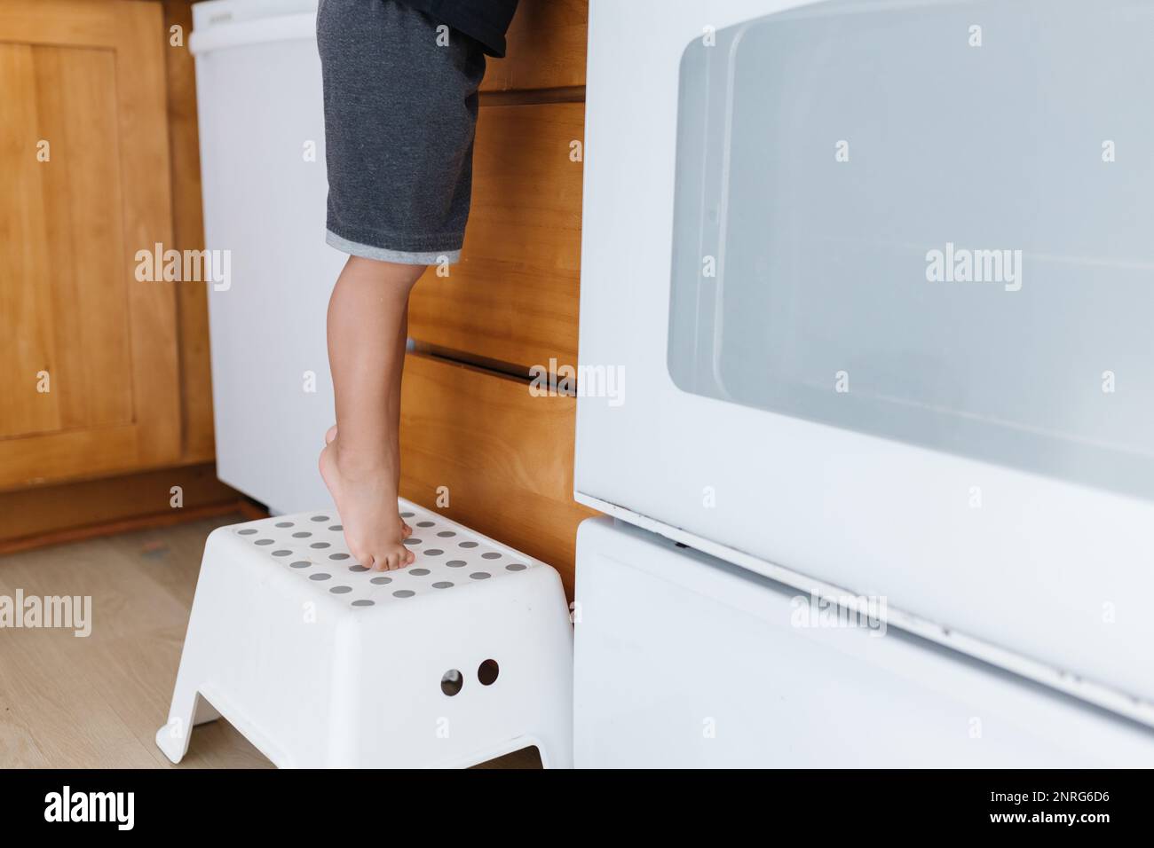 Toddler's tippy toes standing on white stool to reach counter Stock Photo