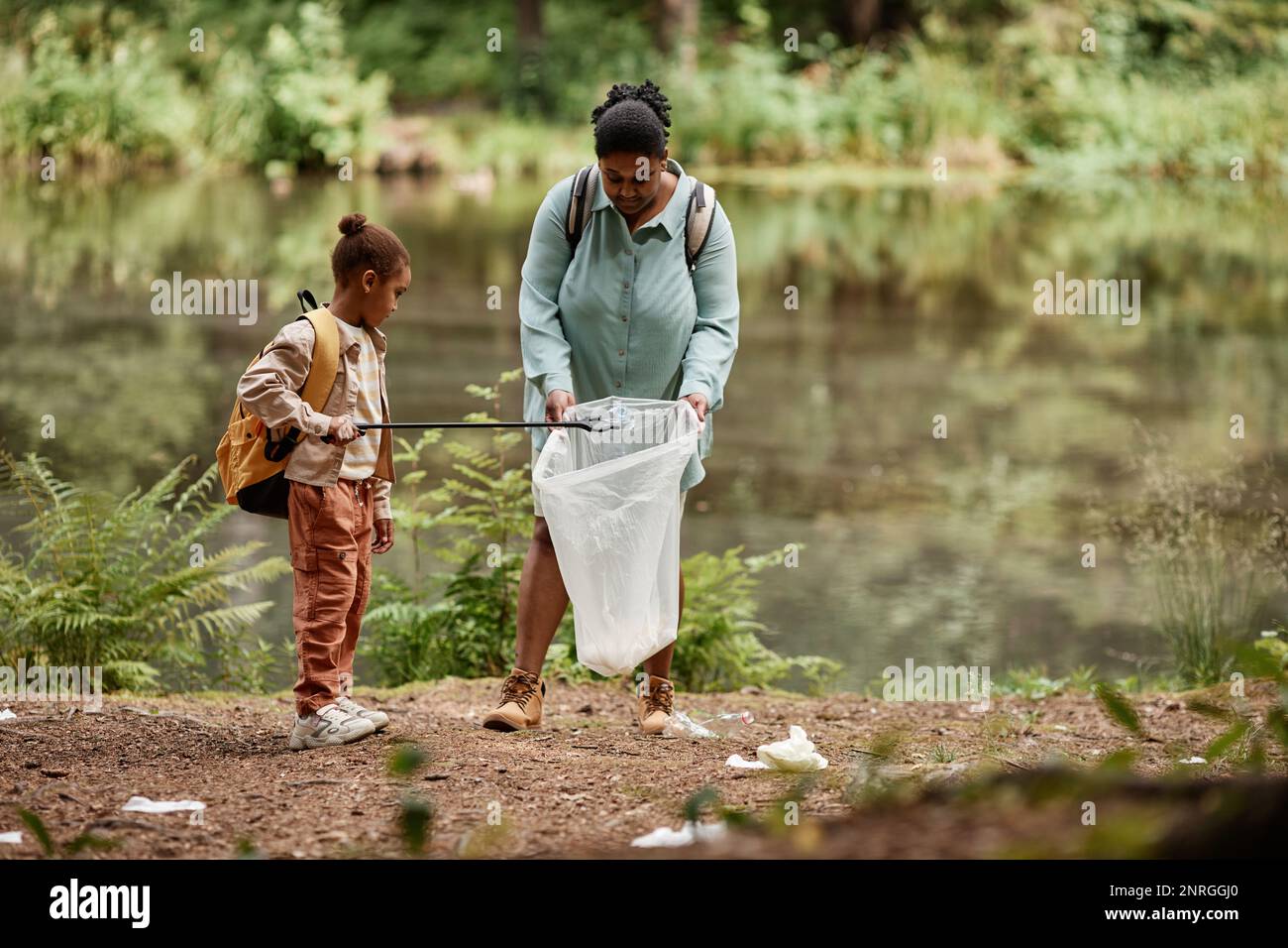 Full length portrait of eco-activist mother and daughter cleaning urban trash by river, copy space Stock Photo