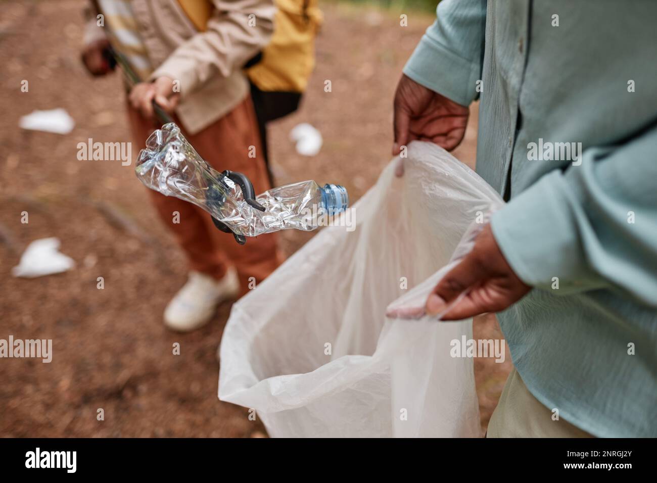 High angle close up of mother and daughter helping clean nature and putting plastic bottle in trash bag outdoors Stock Photo