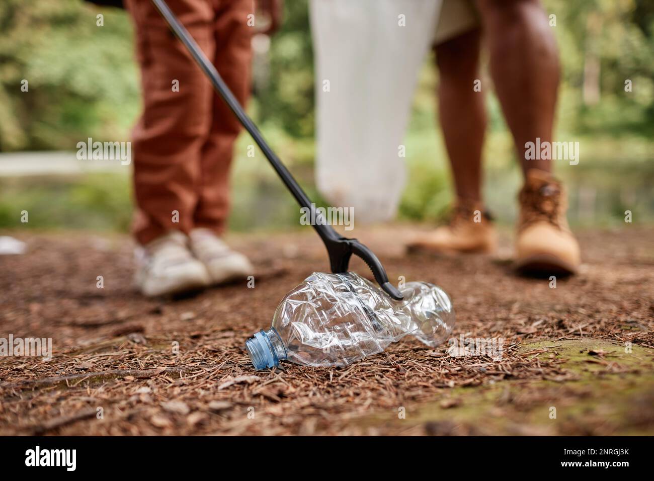 Close up of child picking up plastic bottle outdoors in nature, copy space Stock Photo