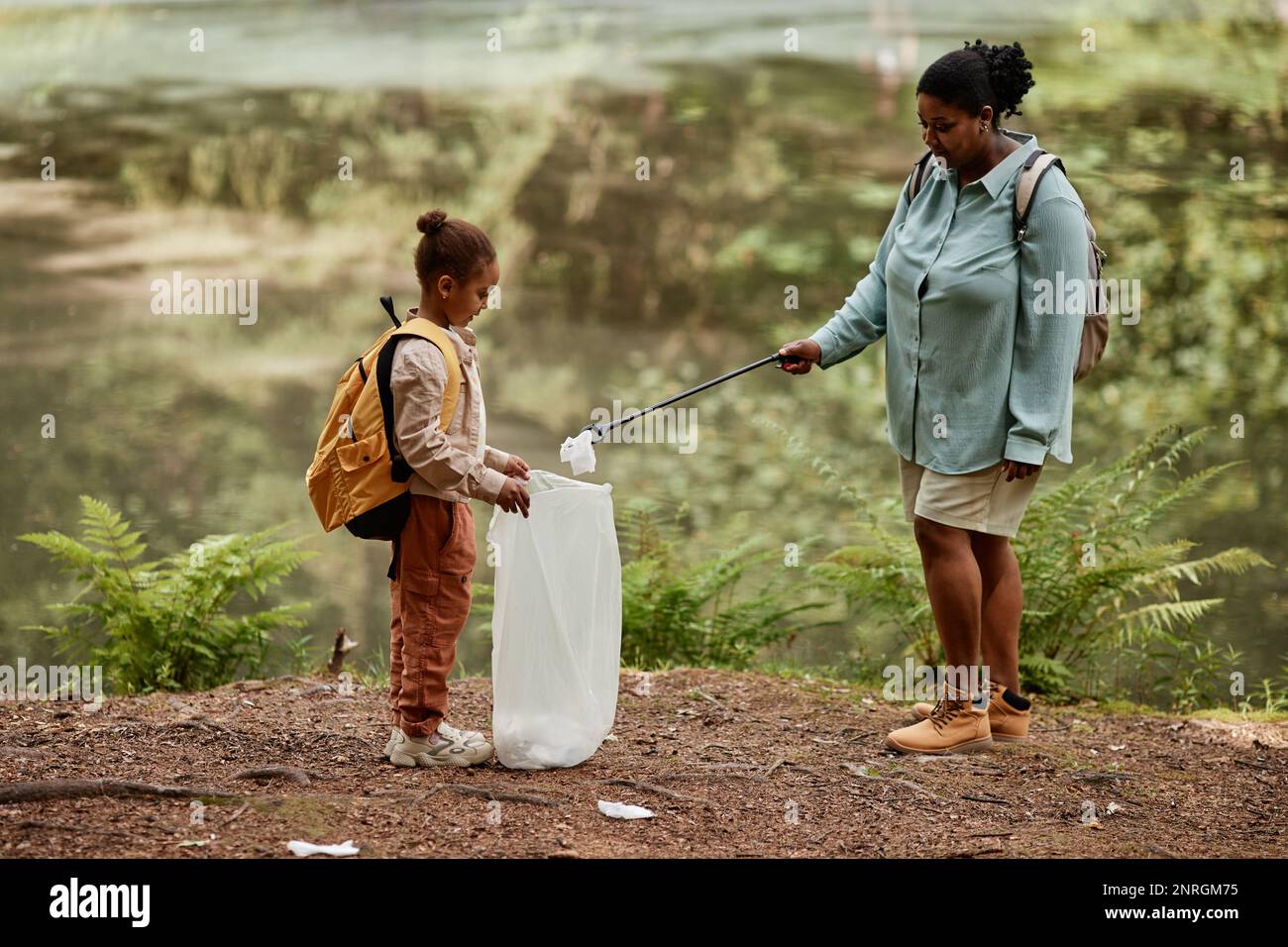 Side view portrait of eco activist mother and daughter helping clean nature and picking plastic bottles outdoors Stock Photo