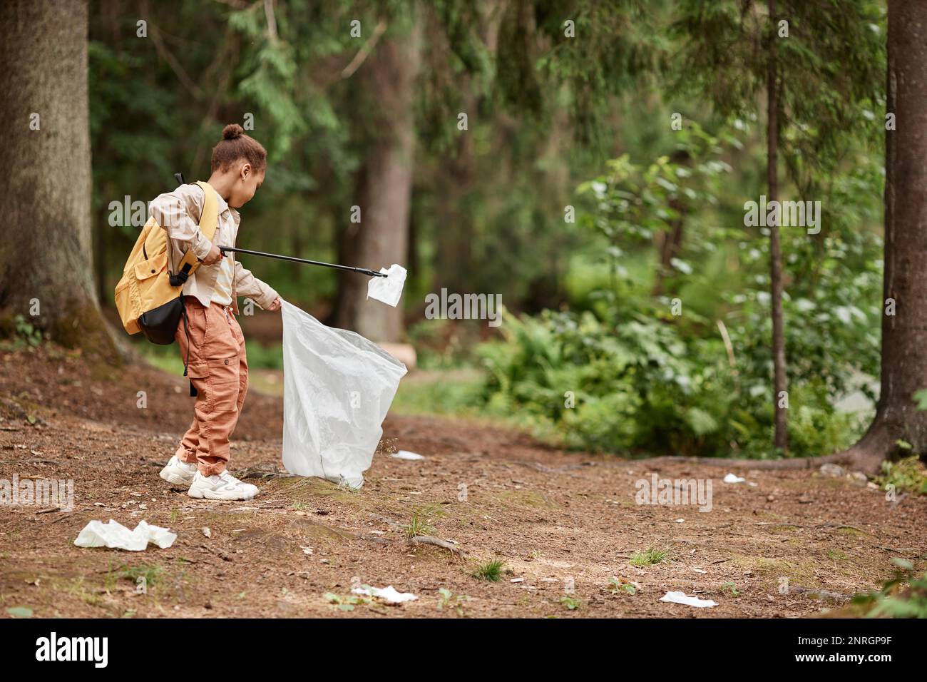 Side view portrait of eco activist little girl picking up plastic bottles in nature trail, copy space Stock Photo