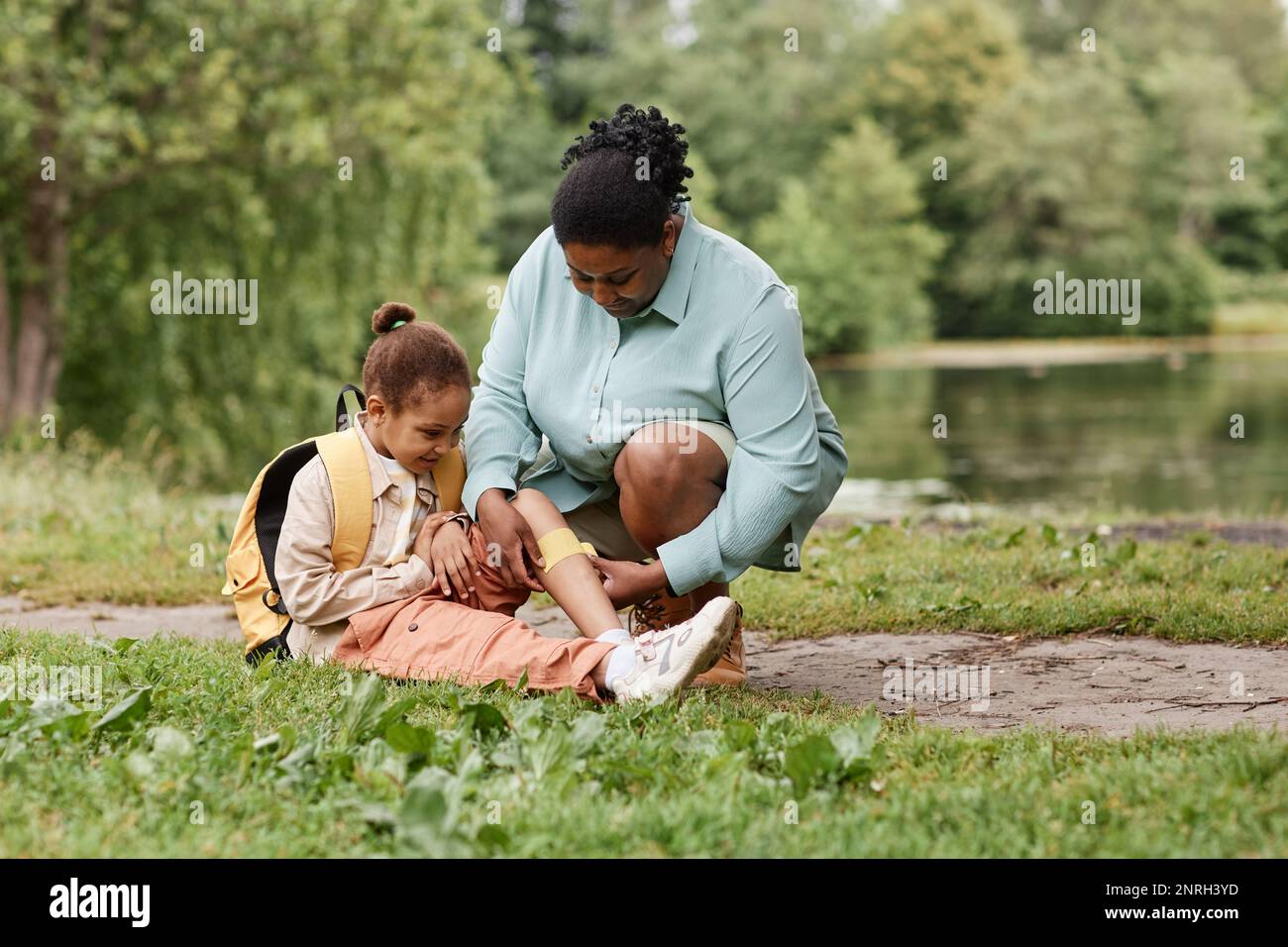 Portrait of caring black mother putting band aid on knee of little girl injured during nature hike, copy space Stock Photo