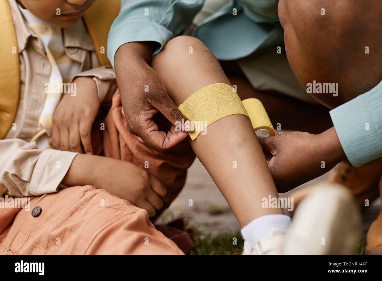 Close up of caring mother putting bandage on childs knee outdoors Stock Photo