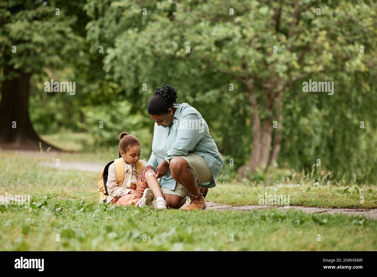 Loving mother putting band aid on knee of little girl injured during nature hike, copy space Stock Photo