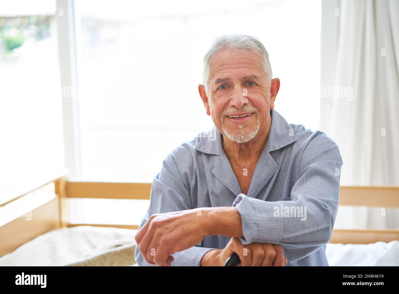 Portrait of smiling senior man wearing sleepwear sitting on bed at retirement home Stock Photo