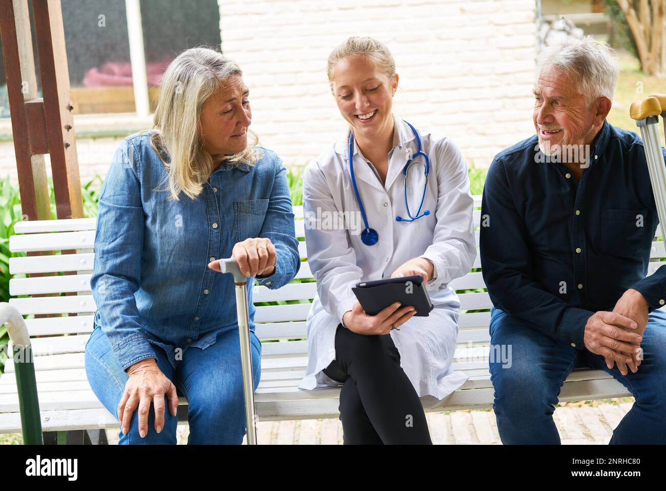 Smiling female doctor explaining elderly woman and man over tablet PC in garden of nursing home Stock Photo