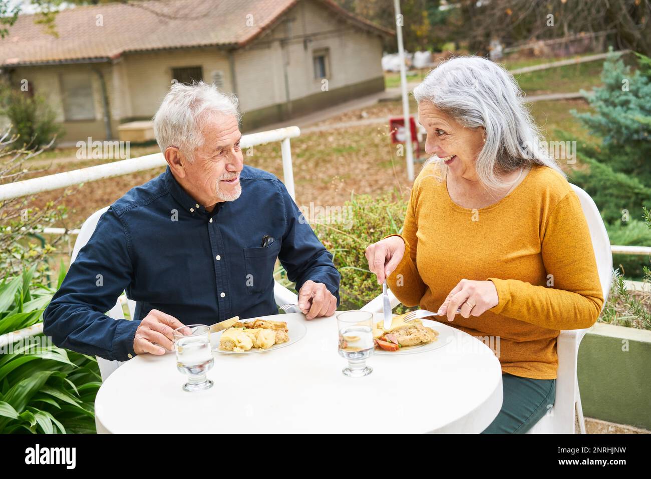 Happy senior man and woman having meal while sitting at table in garden of nursing home Stock Photo