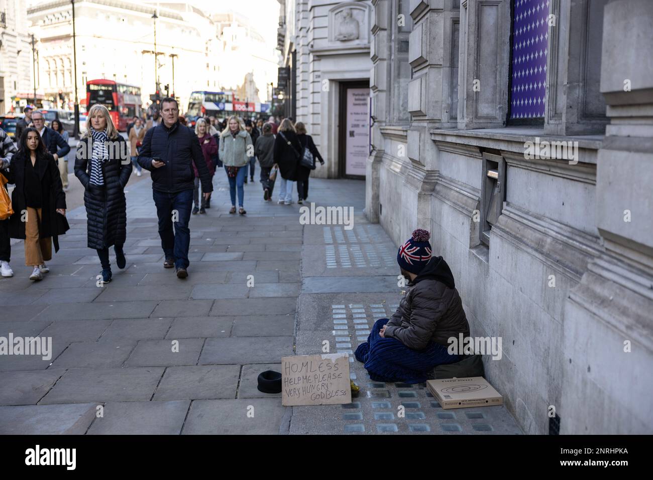 A Homeless man sits on the pavement with a sign asking for help with food or money, Piccadilly, London, England, UK Stock Photo