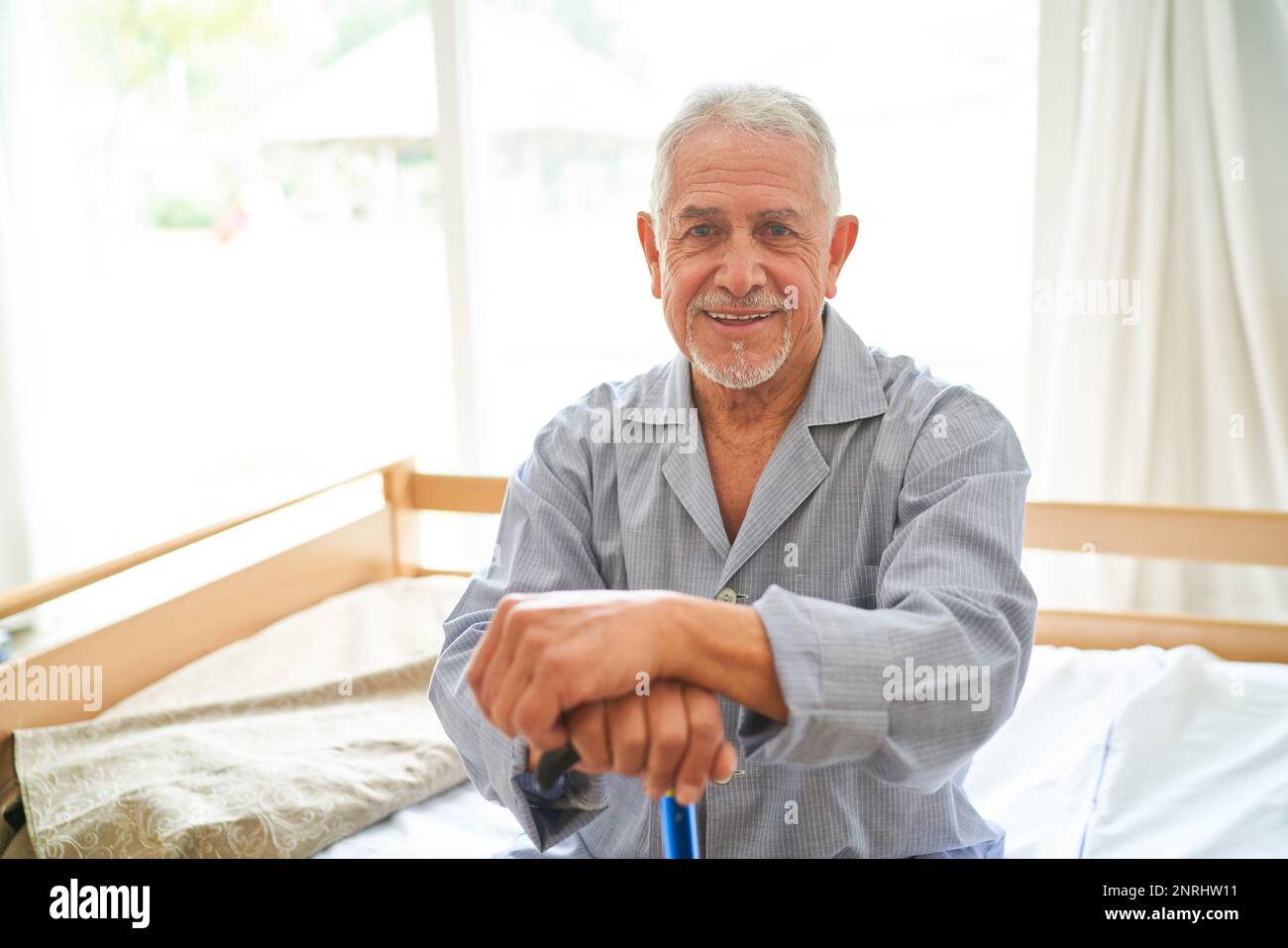 Portrait of smiling senior man in sleepwear sitting on bed at retirement home Stock Photo
