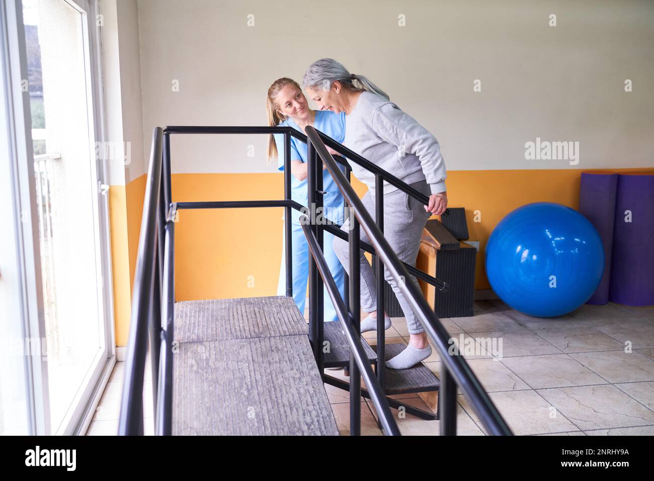 Smiling female physiotherapist assisting senior patient in climbing ...