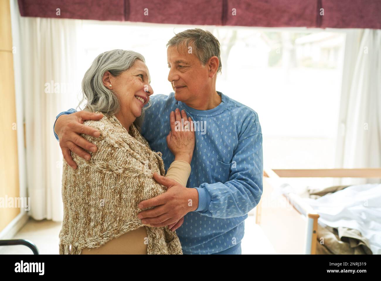 Senior man embracing and looking at smiling woman while standing in nursing home Stock Photo