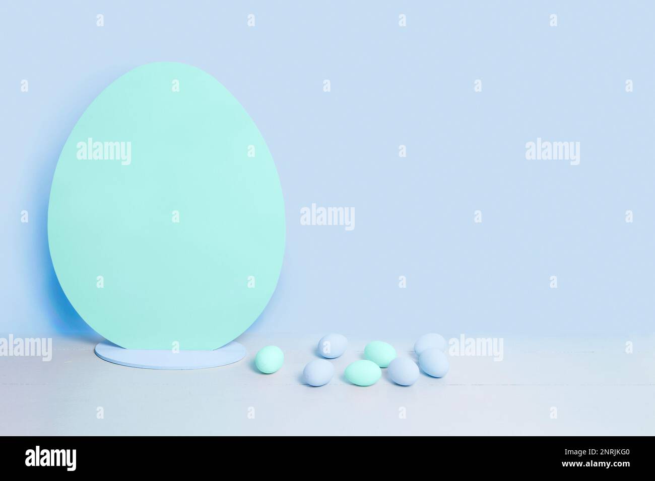 Big blank turquoise Easter egg and small blue and turquoise easter eggs on the background of blank blue wall. Minimalist Easter background Stock Photo
