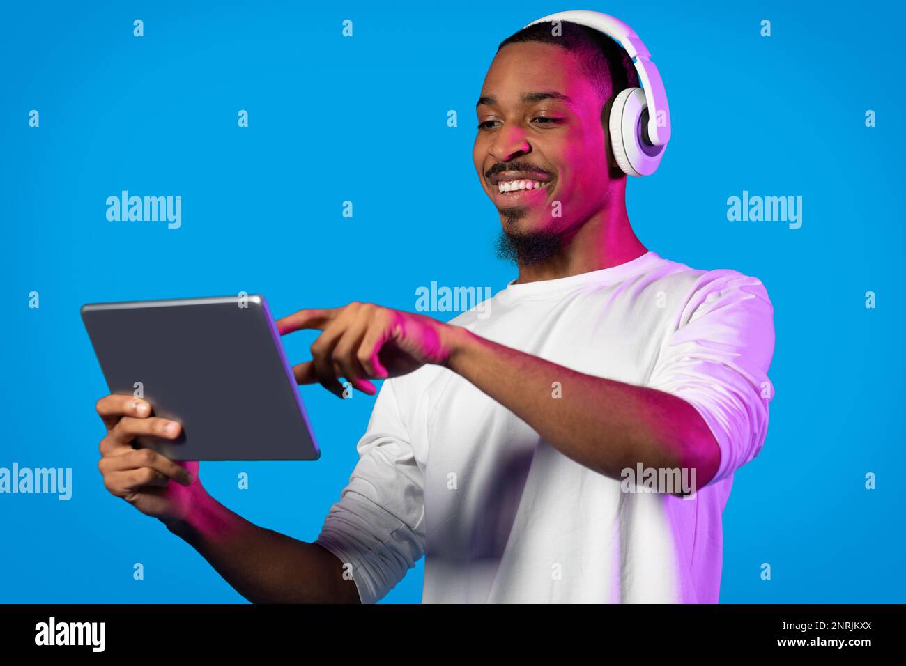 Joyful black guy using modern digital pad and wireless headphones Stock Photo