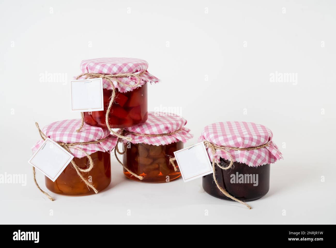 A set of jam jars with pink and white checkered lids and blank labels isolated on a white background Stock Photo