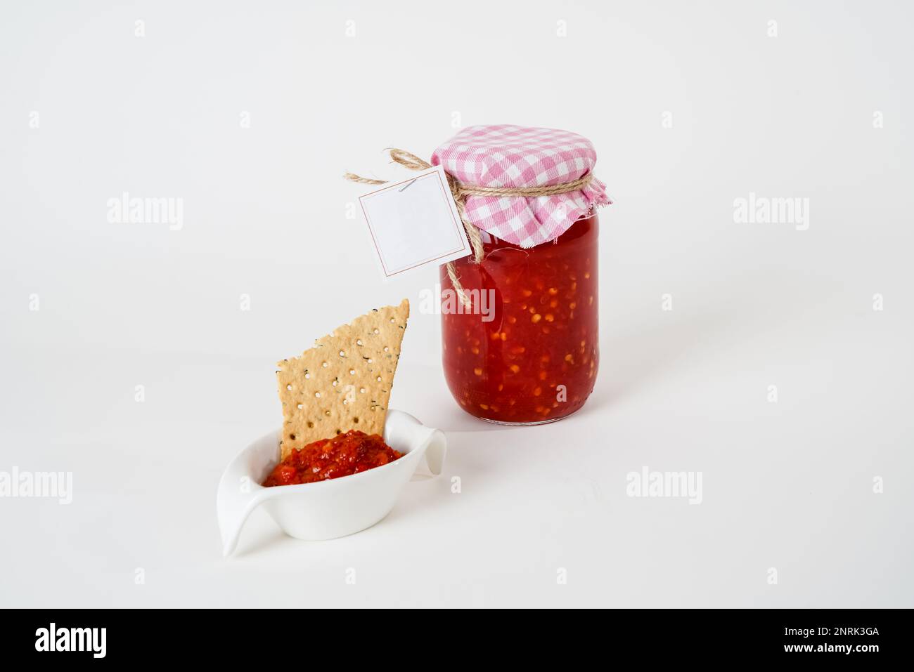 Tomato sauce jar with empty label and small bowl with sauce and cracker