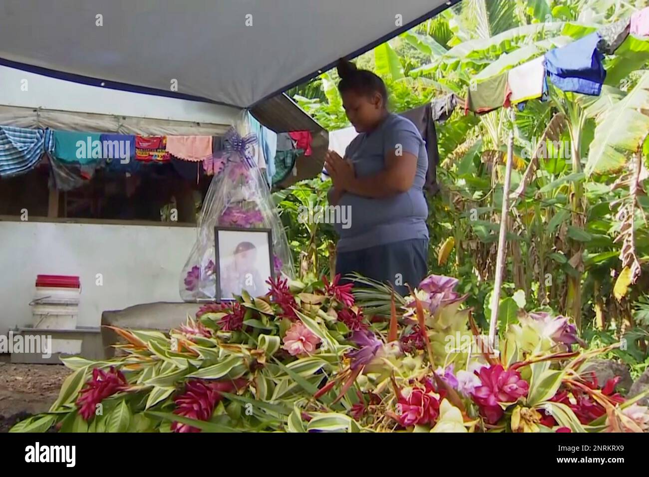 In this November 2019, image from video, a woman prays in front of a portrait of her lost child with measles in Apia, Samoa