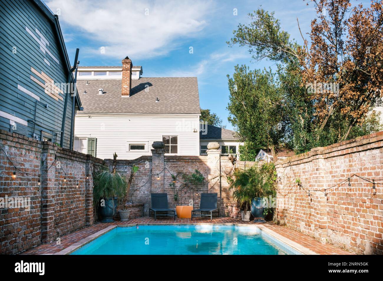 NEW ORLEANS, LA, USA - FEBRUARY 18, 2023: Backyard swimming pool with brick wall and patio furniture and surrounding homes in the background Stock Photo