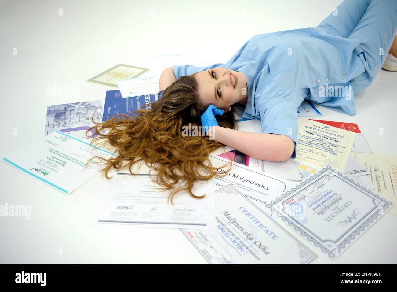 beautiful woman doctor in gloves and blue medical suit lies on diplomas