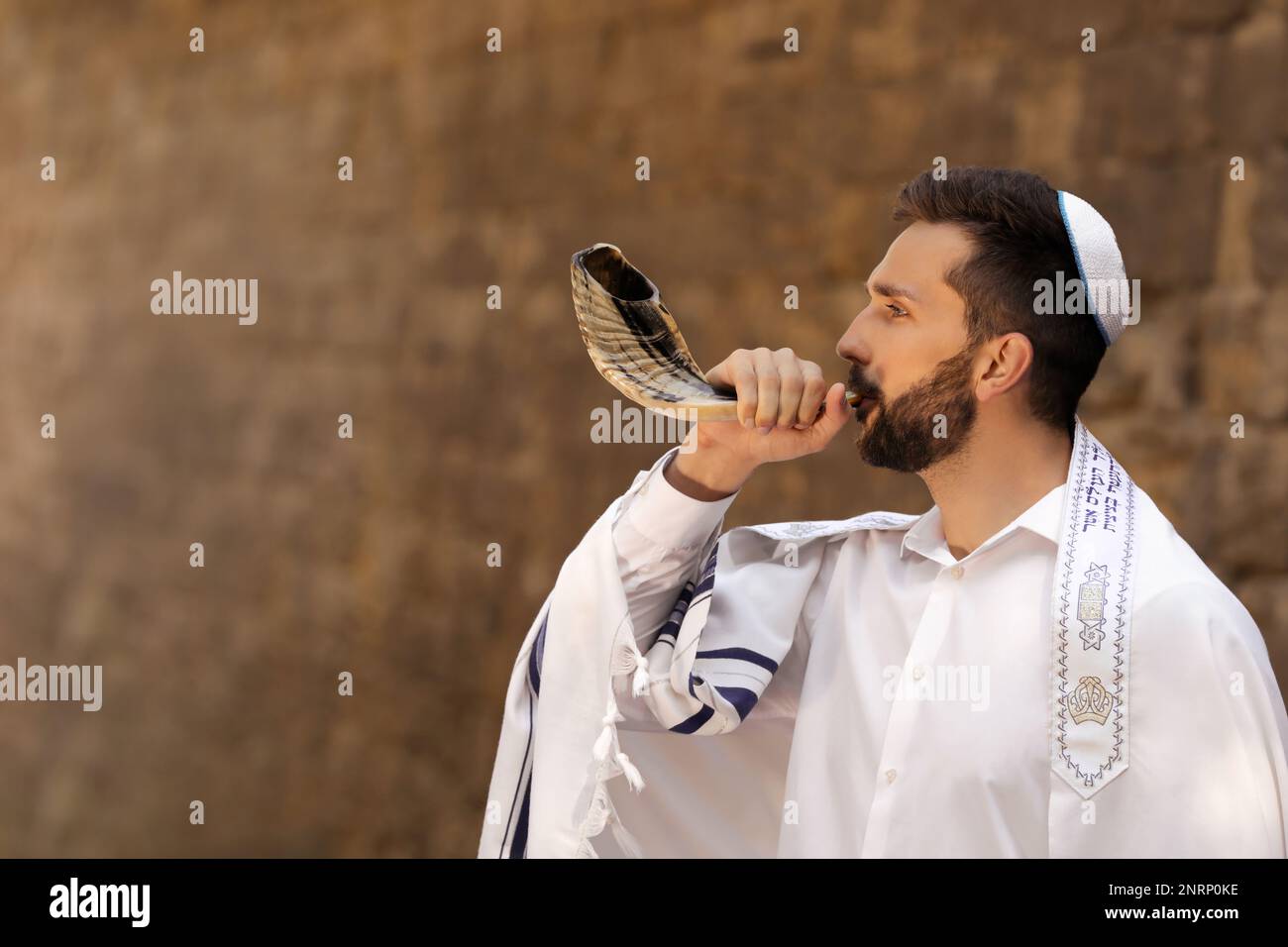 Jewish man blowing shofar on Rosh Hashanah outdoors. Wearing tallit with words Blessed Are You, Lord Our God, King Of The Universe, Who Has Sanctified Stock Photo