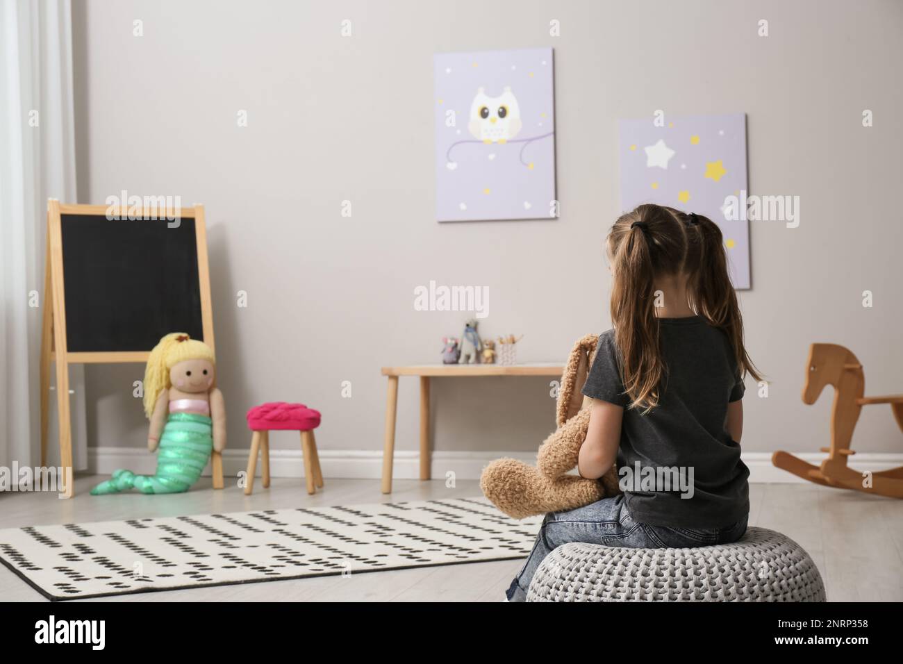 Lonely little girl with toy bunny at home, back view. Autism concept ...