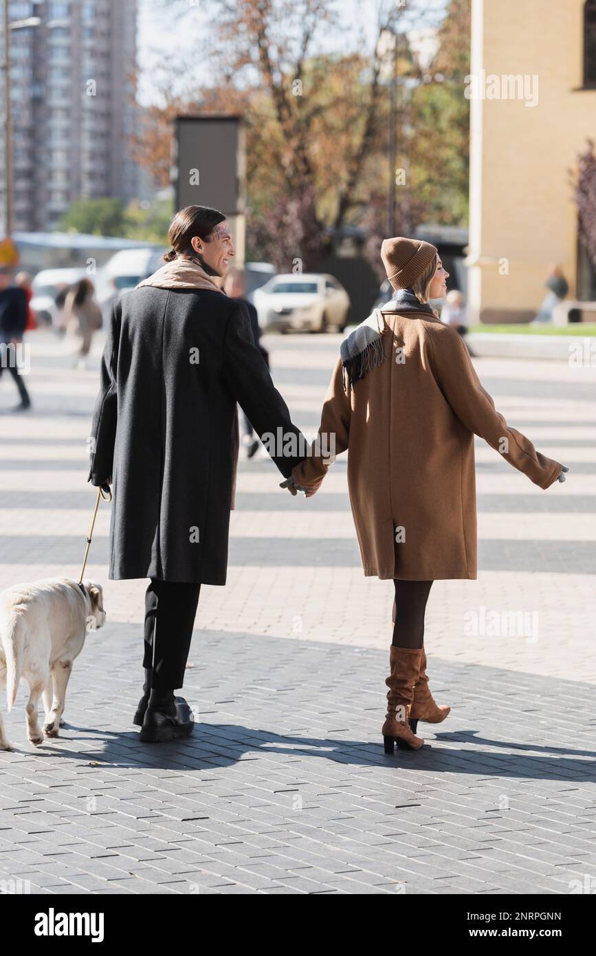 full length of stylish couple in spring clothes holding hands while walking with dog,stock image Stock Photo