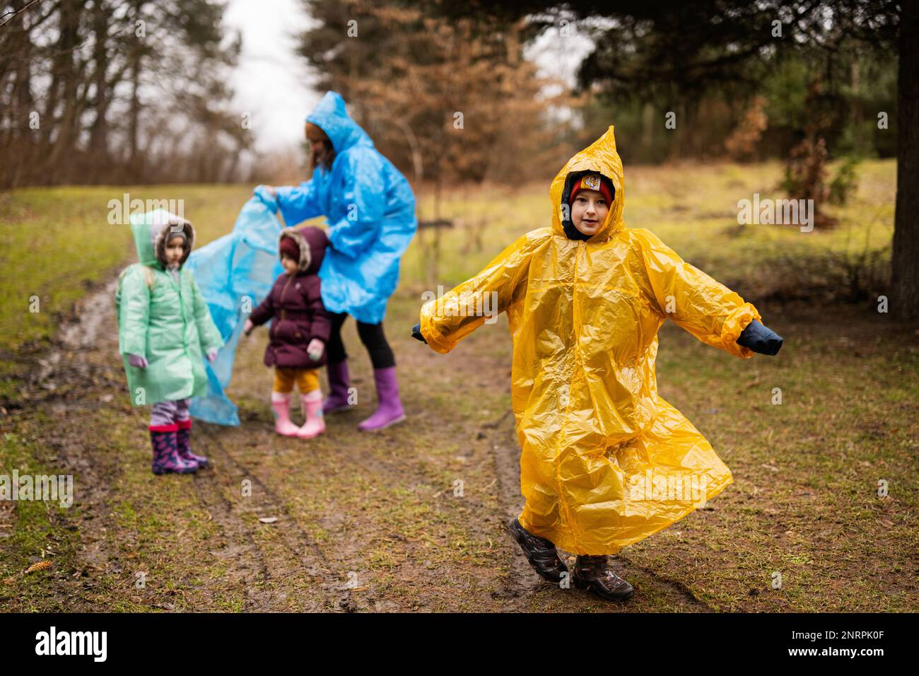 Boy in yellow raincoat against mother and children in the forest after