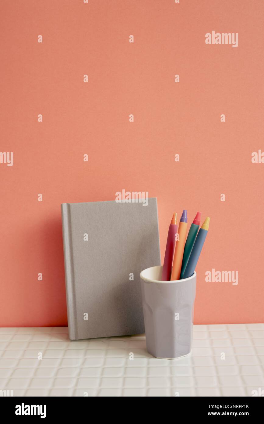 Notebook and pen holder on white desk. pink wall background. workspace