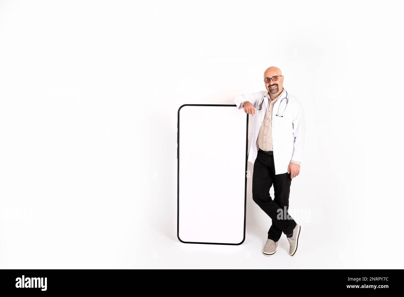 Doctor leaning on big smartphone. Isolated white background. Mobile app advertisement concept idea. Full body length of male doctor with empty screen Stock Photo