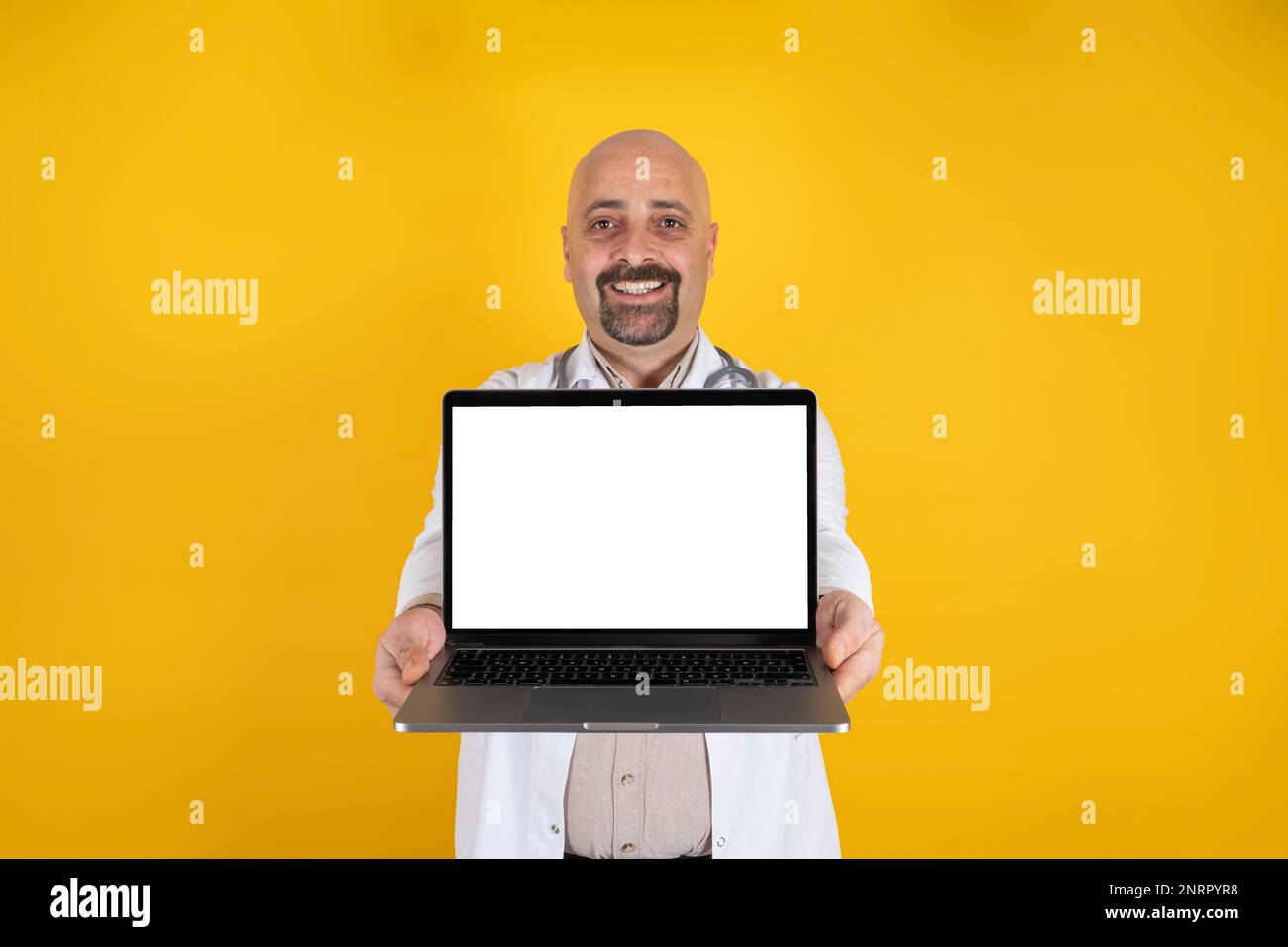 Cheerful caucasian man doctor showing laptop. White blank screen for mock up. Isolated on warm orange studio background with copy space. Stock Photo