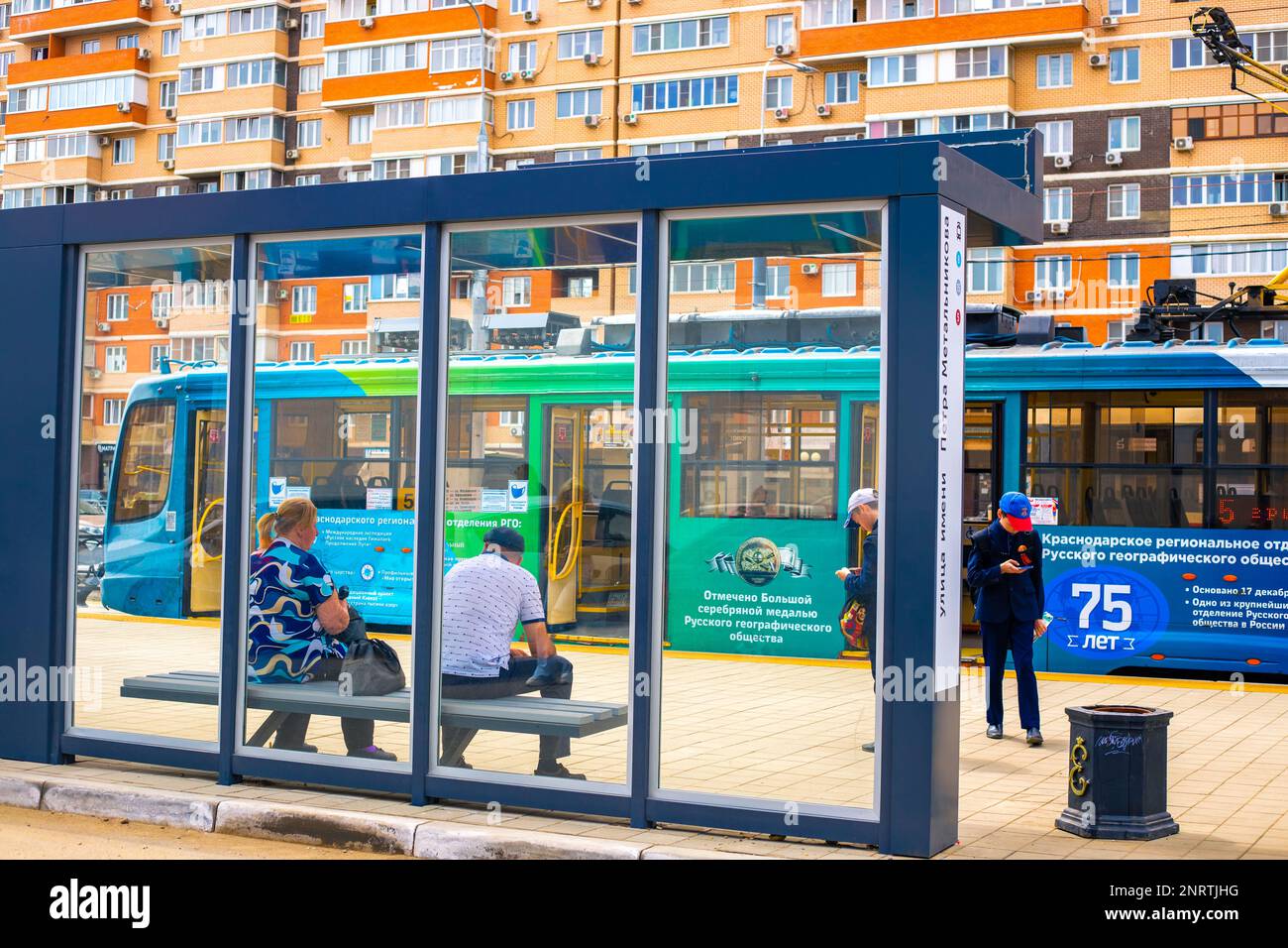 People waiting for a streetcar at a transparent streetcar stop in Krasnodar, Russia-28.04.2022 Stock Photo