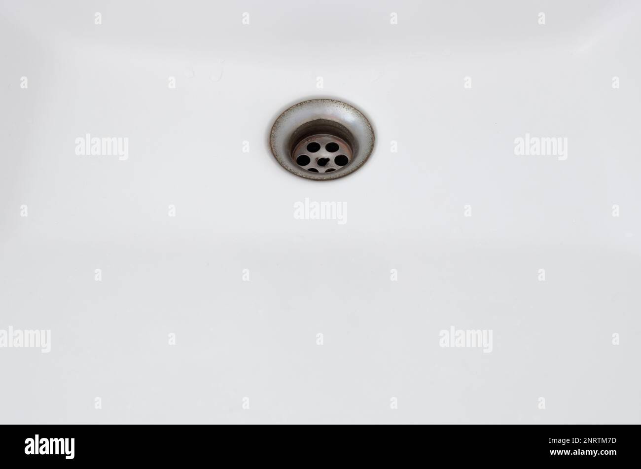 The rusty sinkhole in the white basin of the public toilet in the urban