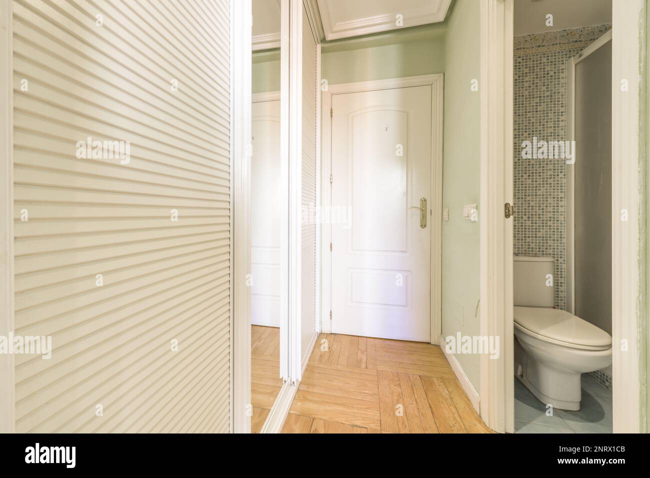 A bedroom walk-in wardrobe with sliding mirror doors and white Venetian wood next to an en-suite toilet Stock Photo