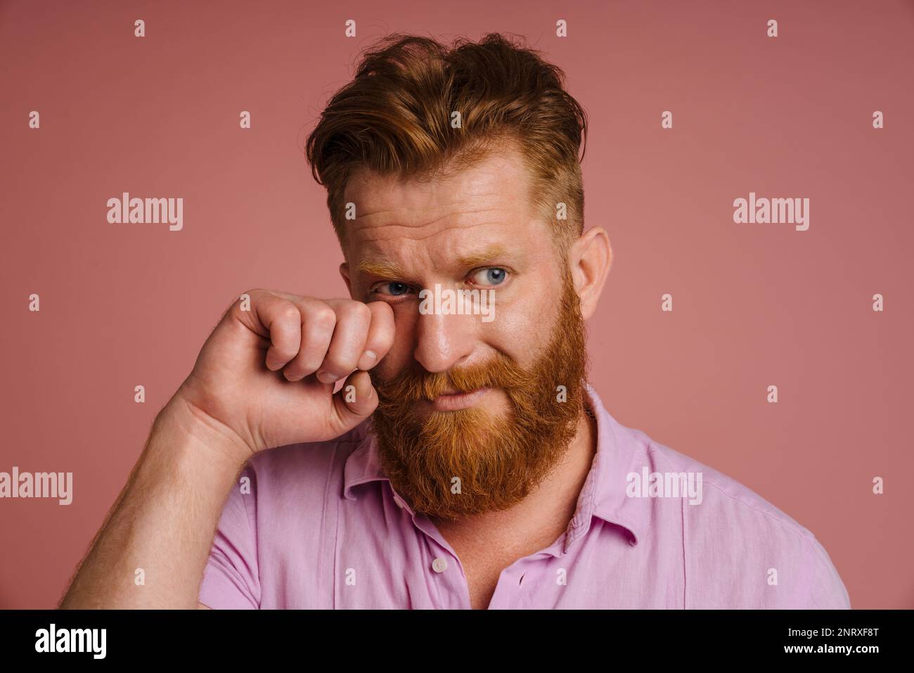 Ginger white man with beard crying while wiping his tears isolated over pink background Stock Photo