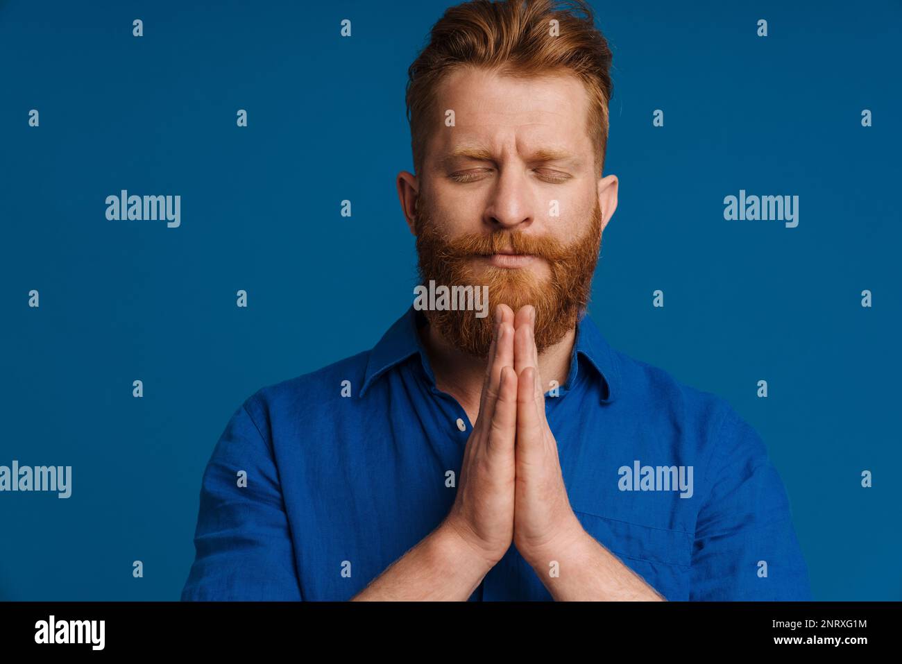 Ginger white man making pray gesture while posing with eyes closed