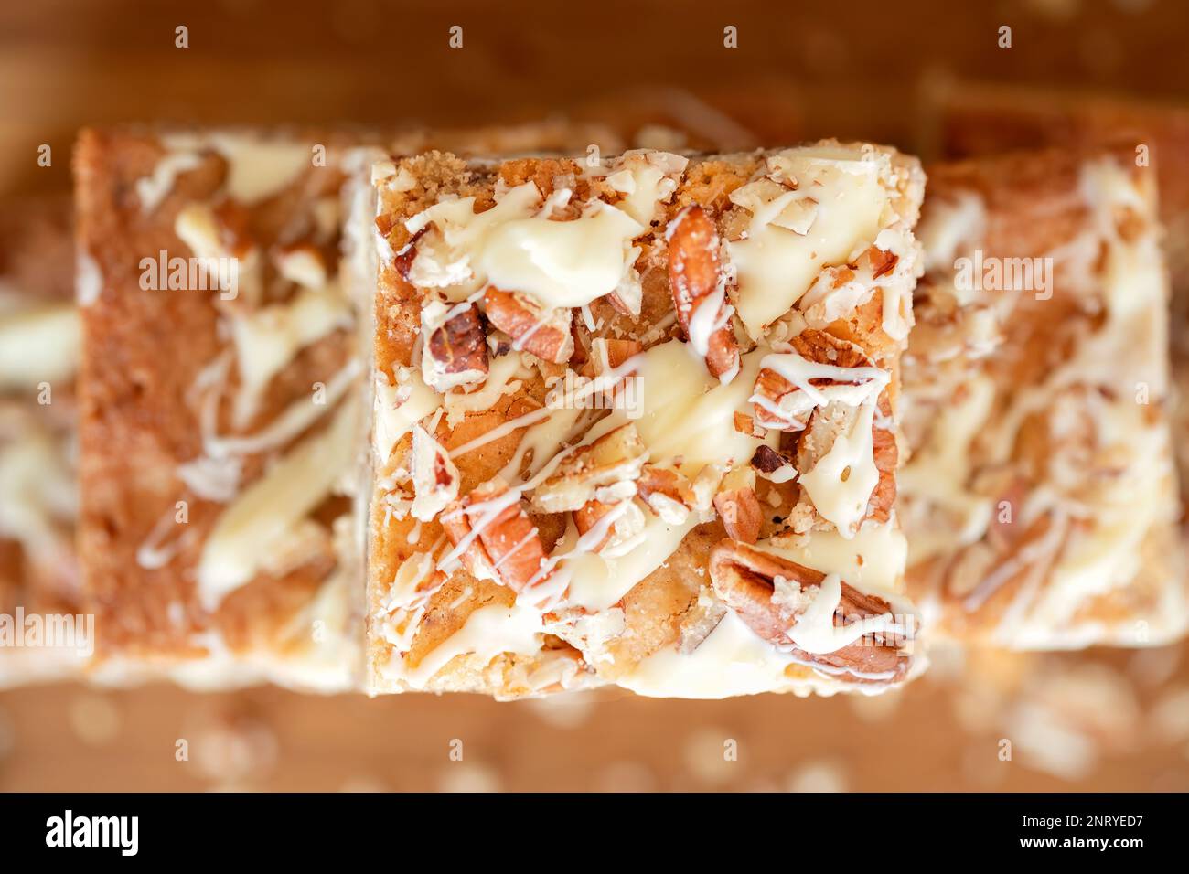 A overhead view of home baked white chocolate pecan Blondies arranged on a wooden platter. The blondies are still warm and gooey. an indulgent treat Stock Photo