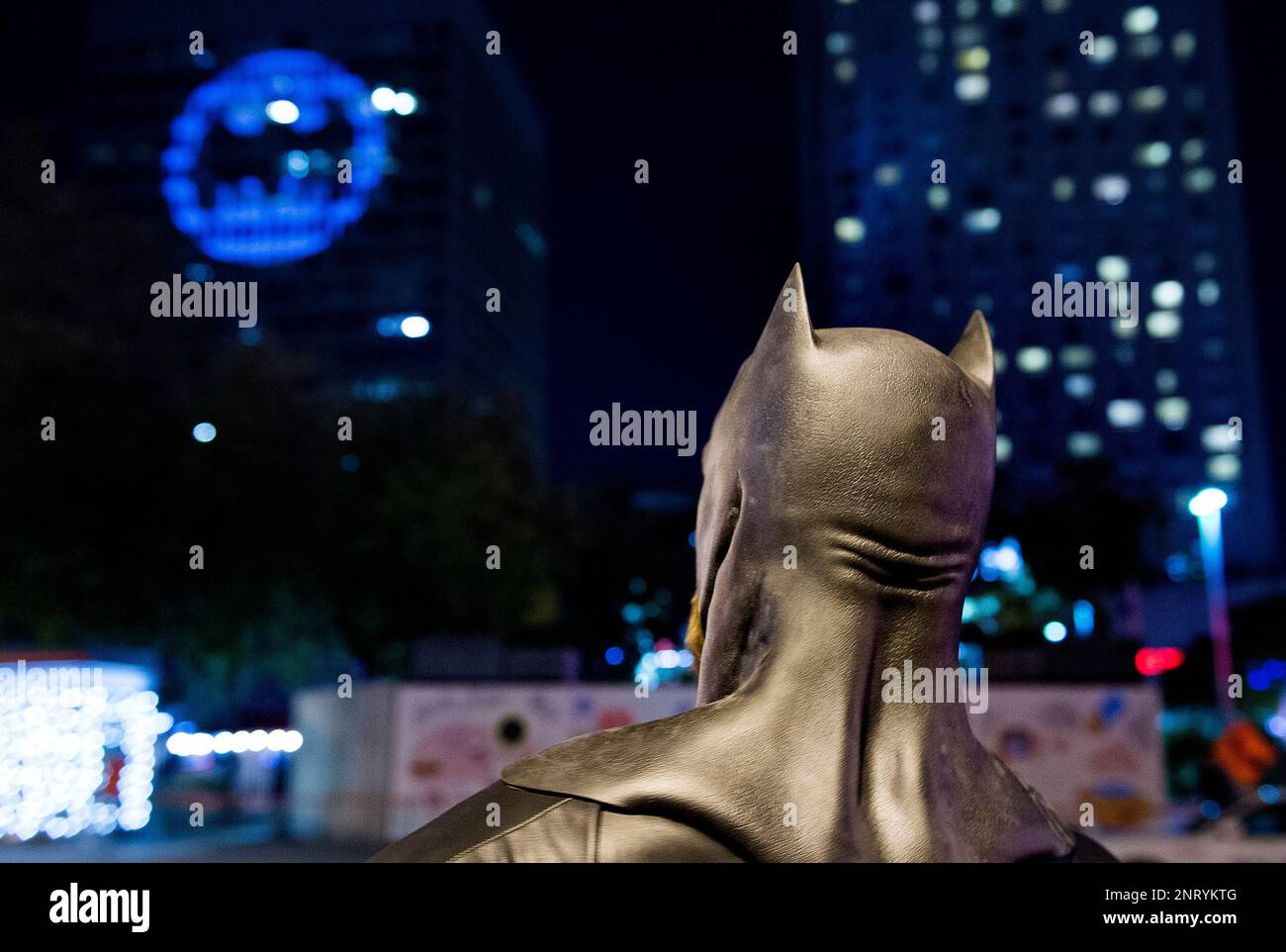 A man dressed as Batman looks up towards the Batman signal projected ...