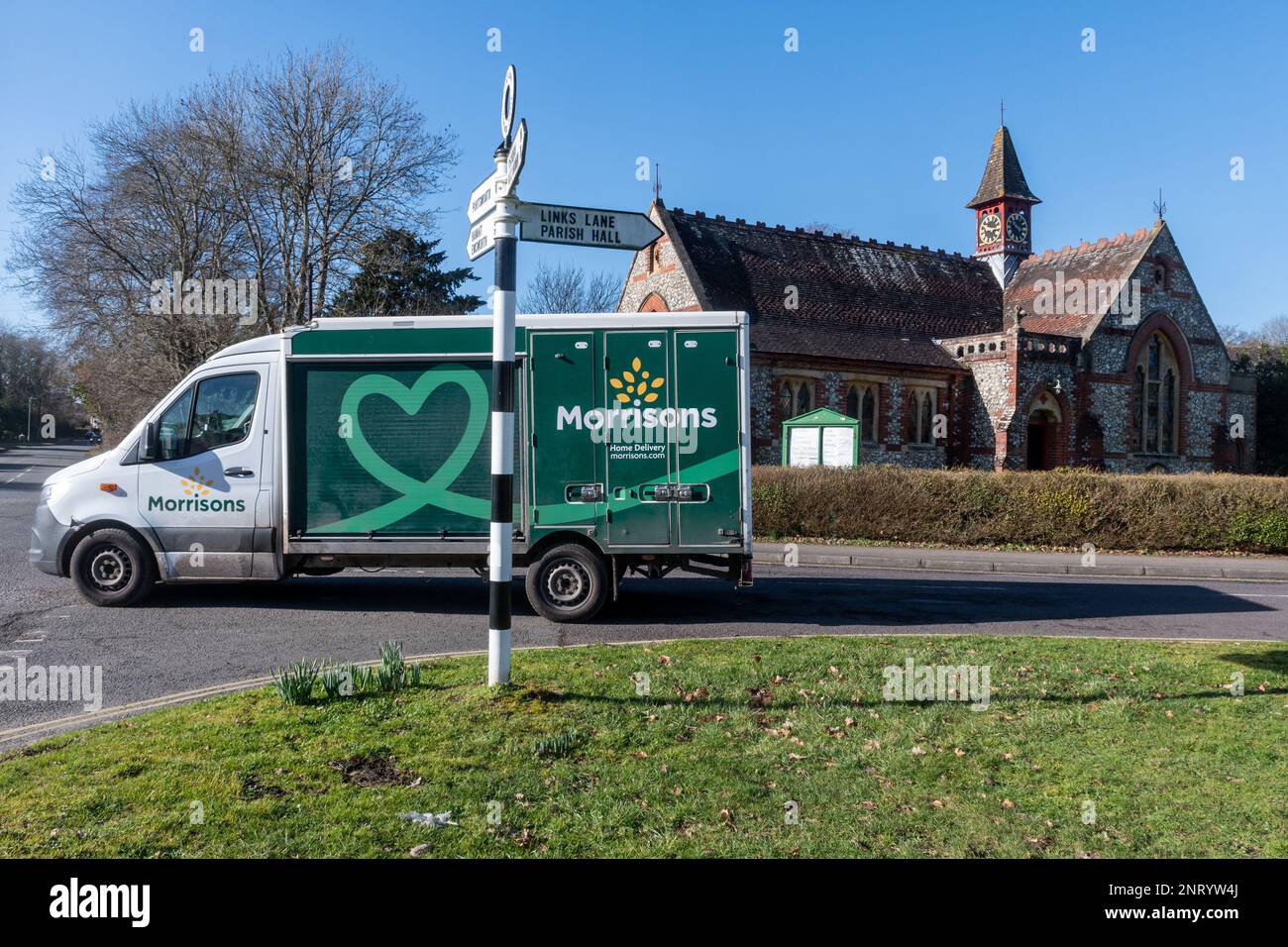 Morrisons supermarket delivery van driving through Rowlands Castle in front of the village church, Hampshire, England, UK Stock Photo