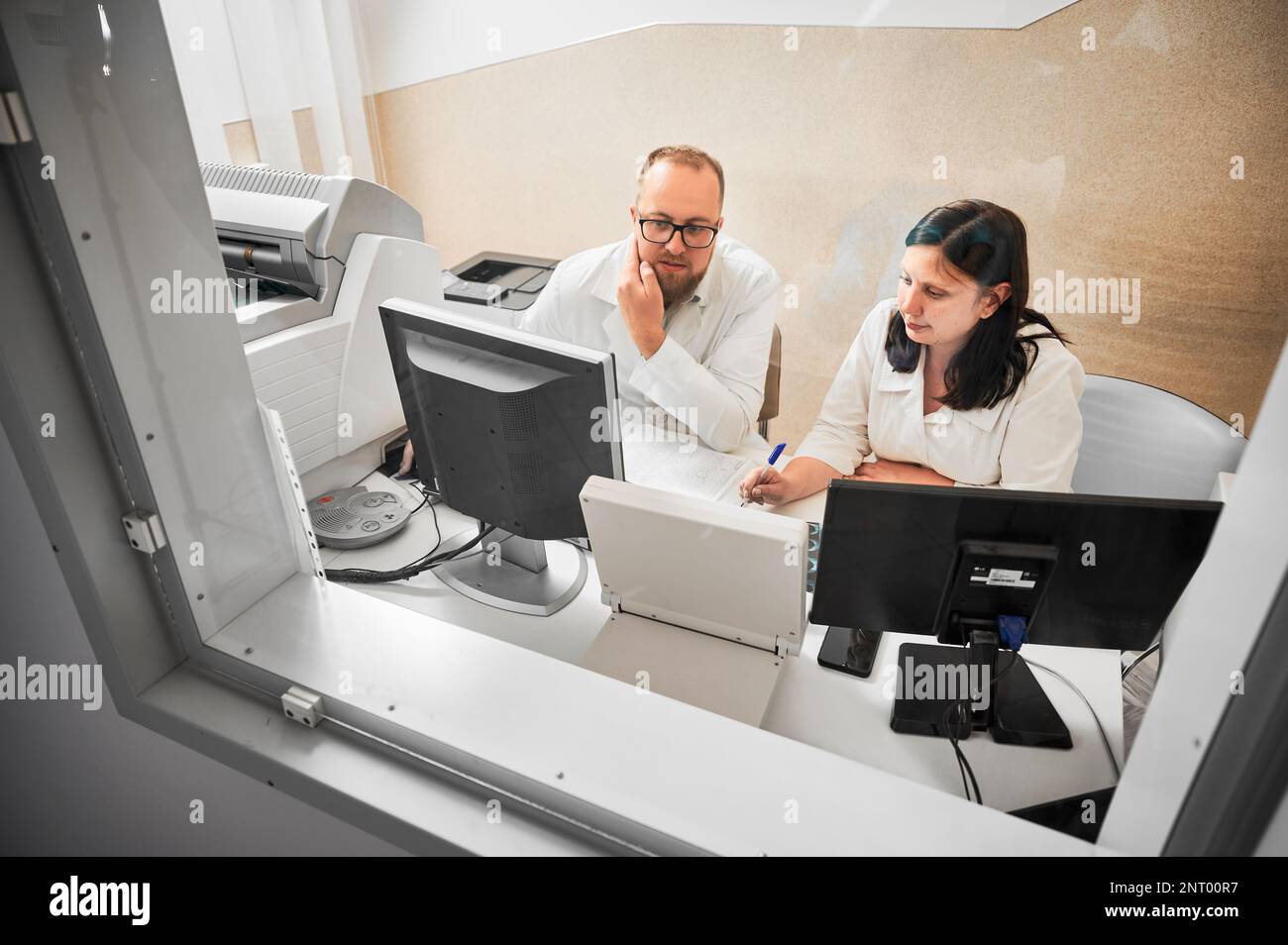 Medical computed tomography or MRI scanner. Side view of two specialists sitting at computer, working in hospital. Doctors looking at MRI results. Concept of medicine and healthcare. Stock Photo