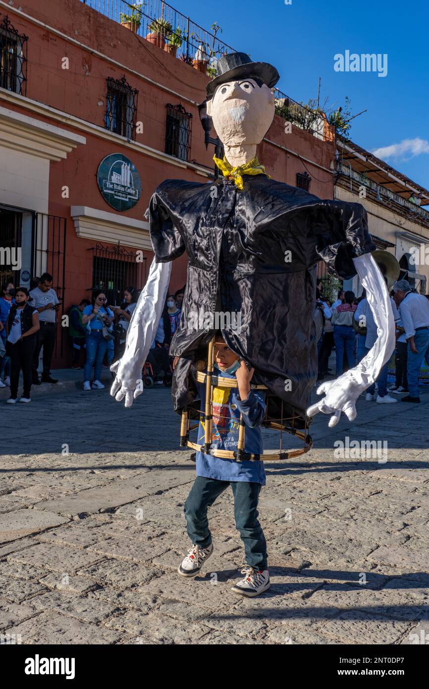 A young boy carrying a mono de calenda or giant puppet dances in the Santo Domingo Plaza in Oaxaca, Mexico.  Mono de calenda translates to parade monk Stock Photo