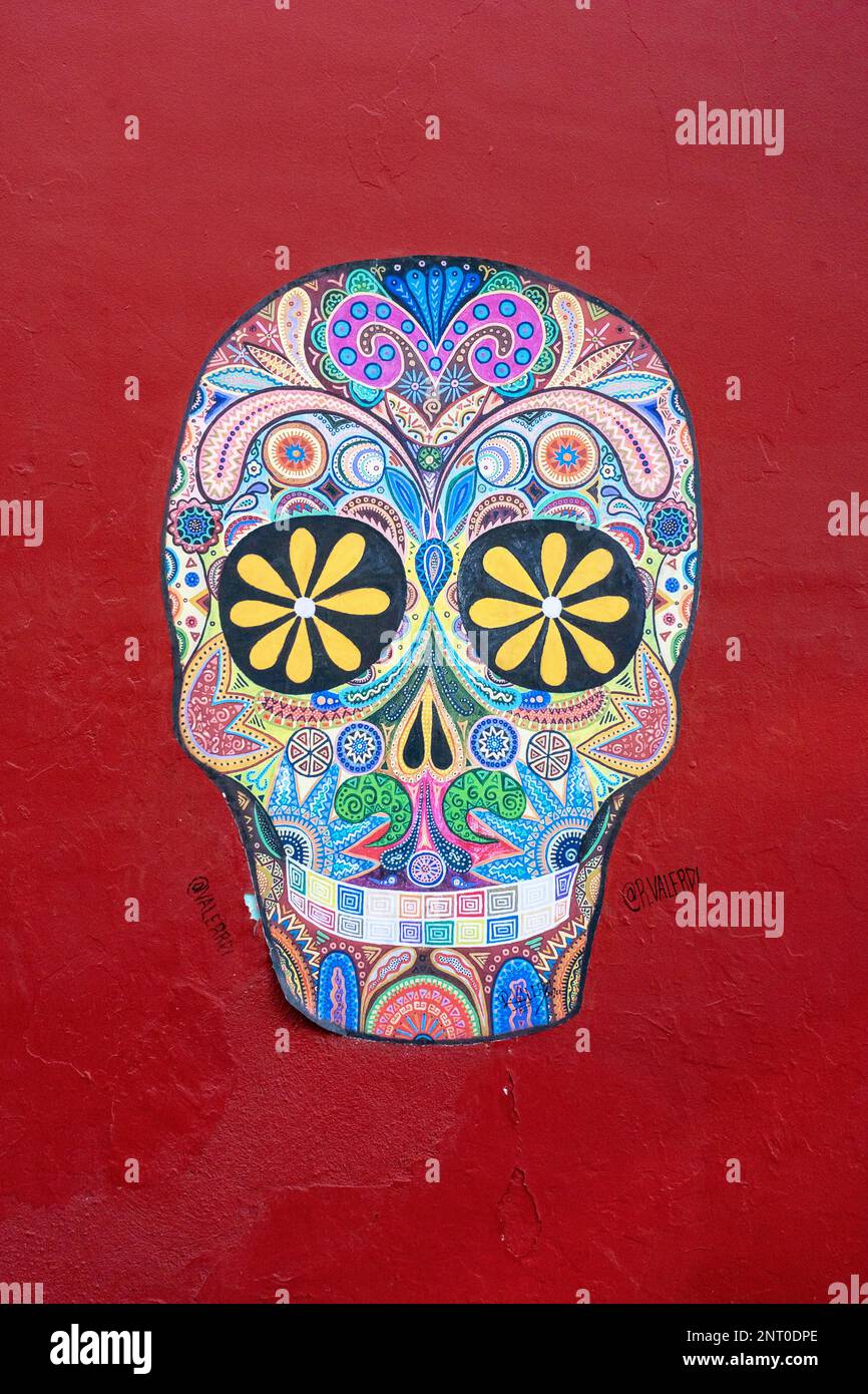 An alebrije-style painting of a skull for Day of the Dead on a red wall in historic Oaxaca, Mexico. Stock Photo