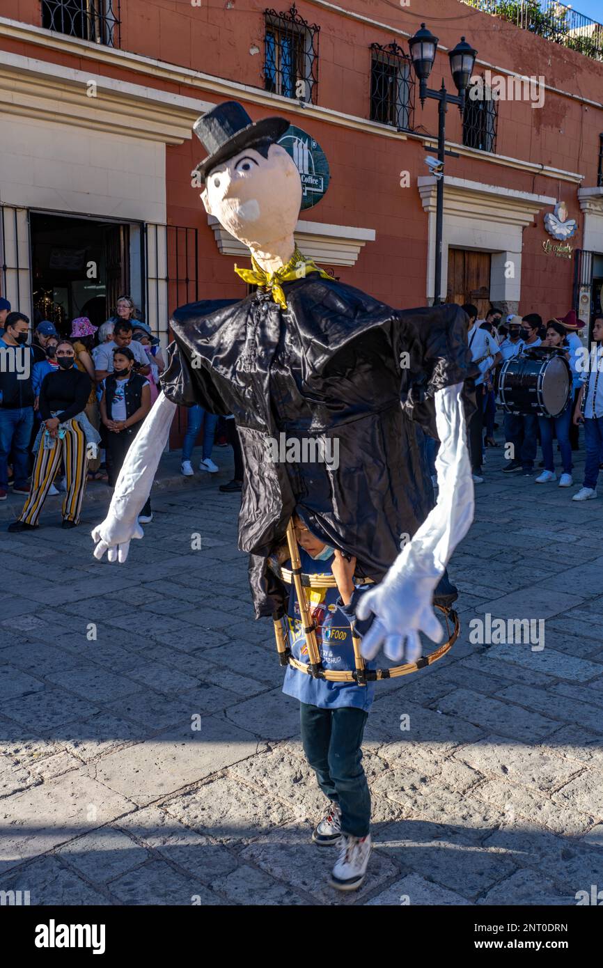 A young boy carrying a mono de calenda or giant puppet dances in the Santo Domingo Plaza in Oaxaca, Mexico.  Mono de calenda translates to parade monk Stock Photo