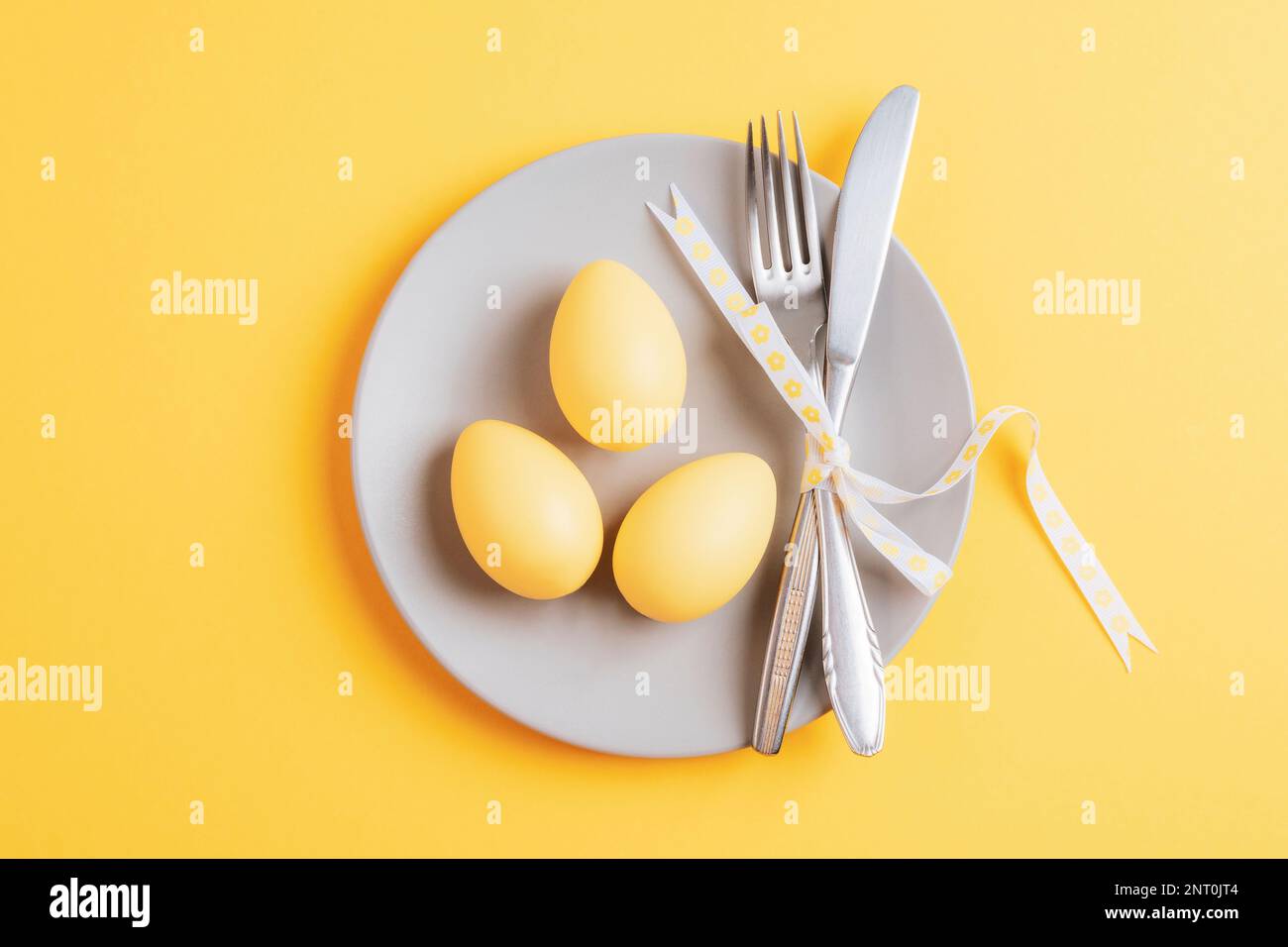 Gray plate with easter painted eggs on yellow background. Happy Easter card. Top view, flat lay. Stock Photo