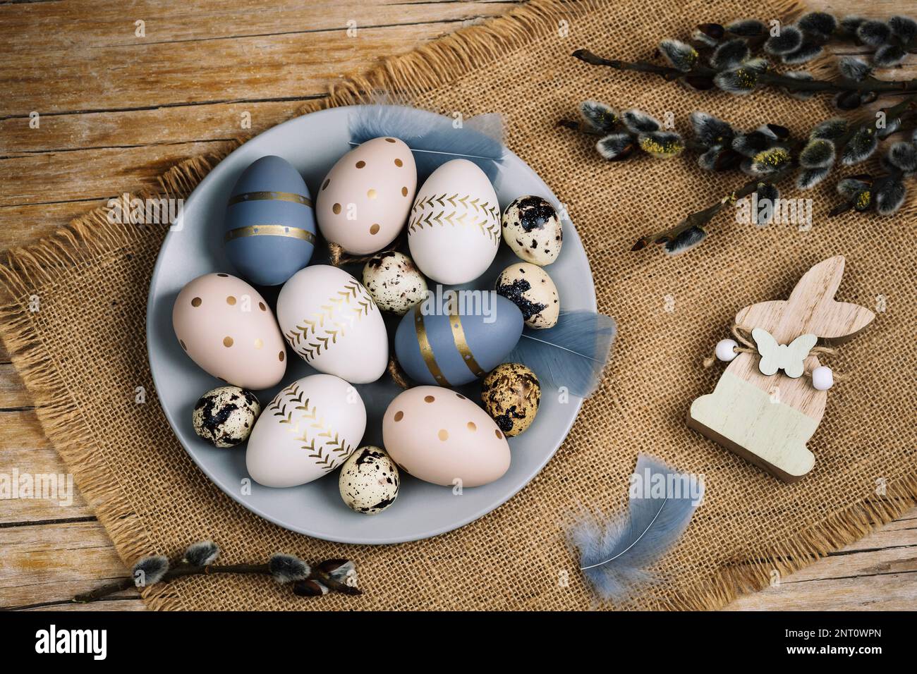 Gray plate with painted Easter eggs and willow branches on a wooden table. Easter greeting card. Top view, flat lay. Stock Photo