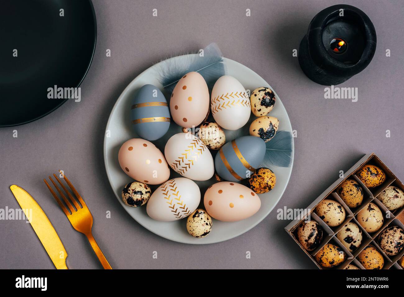 Gray plate with painted Easter eggs, candle and fork and knife on a gray background. Easter table setting. Top view, flat lay. Stock Photo