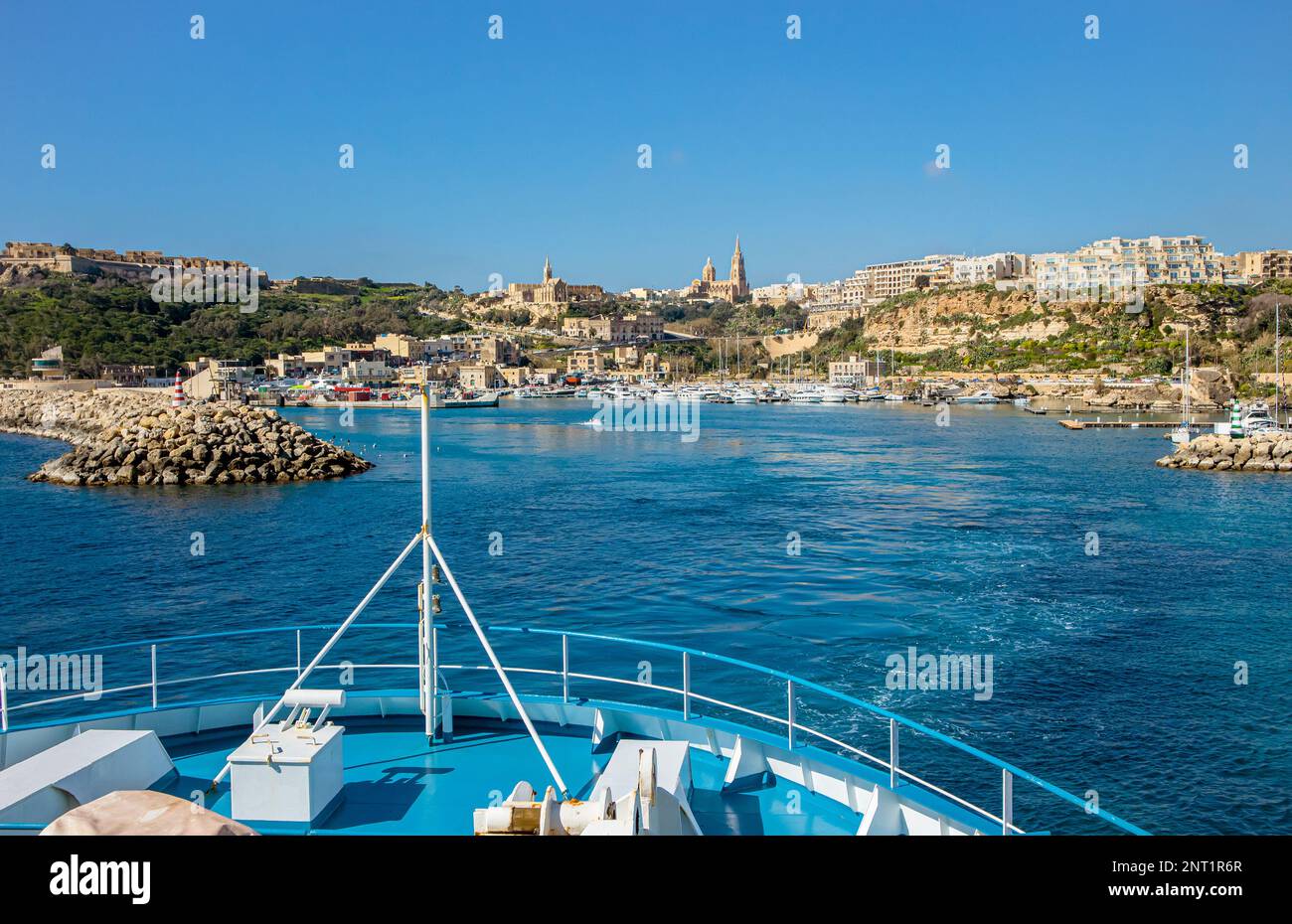 The ship arrives at the port of Mġarr on the island of Gozo, Malta. Beautiful city on the cliffs and hills on the background on sunny spring day. Stock Photo