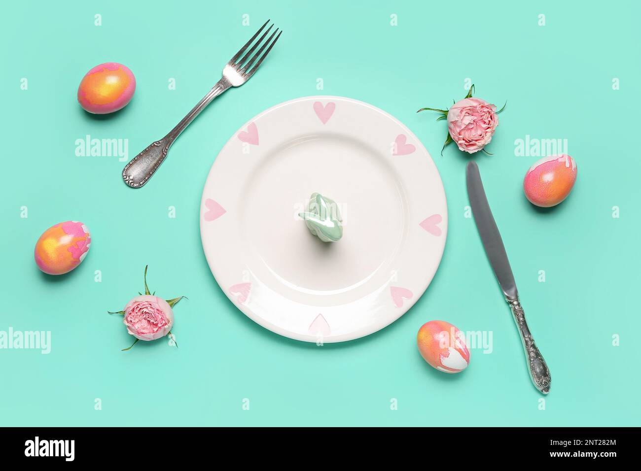 Table setting with Easter rabbit, eggs and flowers on mint background Stock Photo